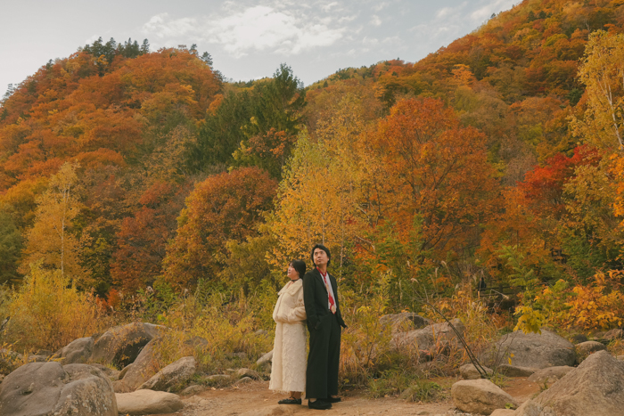 紅葉の山々を背景にポーズをとる2人